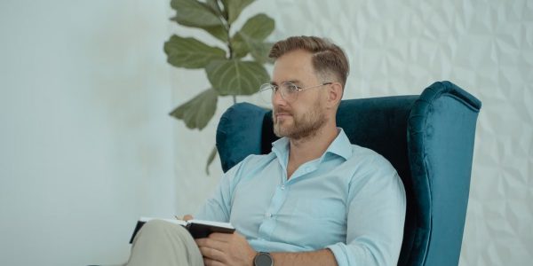 Male counselor in a modern office chair taking notes, promoting mental health awareness.